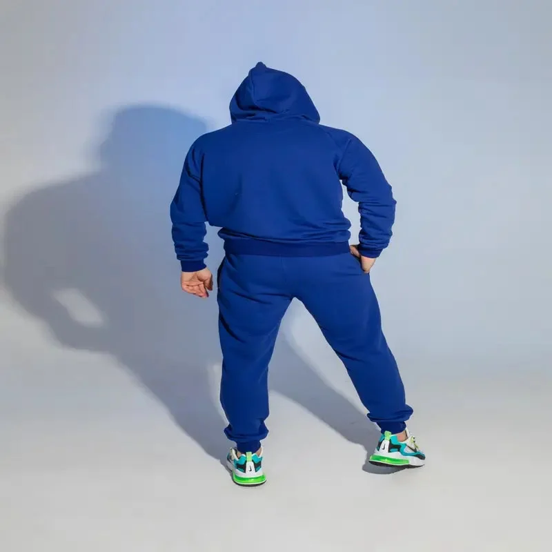 male wearing navy blue tracksuit facing wall with white background designed by men's tracksuit manufacturer
